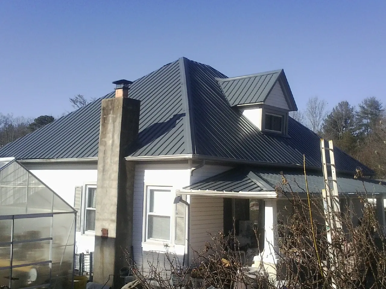 Dark blue standing seam metal roof on a white farmhouse with dormer — Slate & Tile Roof Repair by Roofing Brothers in Stahlstown