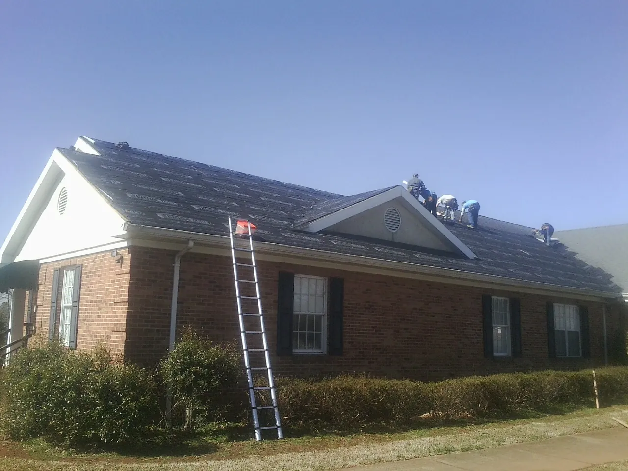 Crew tearing shingles off a brick ranch roof with a ladder set — Emergency Roof Repair work by our crew in Stahlstown