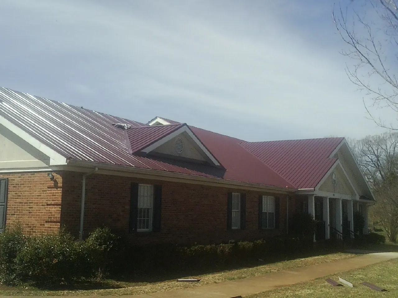 Red metal roof with gabled entries on a long brick building, from a Hail Damage Roof Repair job in Stahlstown