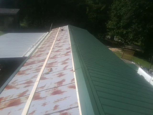 Old rusted panels beside newly installed green metal roofing — Wind Damage Roof Repair by Roofing Brothers in Stahlstown