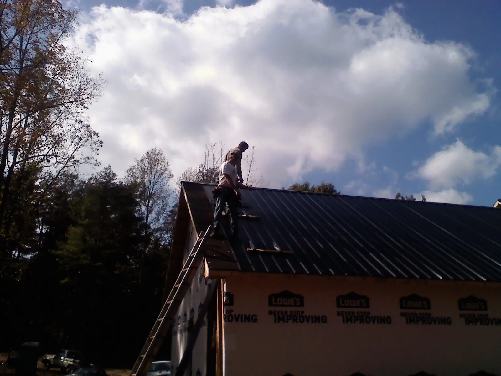 Roofer fastening dark metal panels high against a cloudy sky, from a Roof Inspection job in Stahlstown