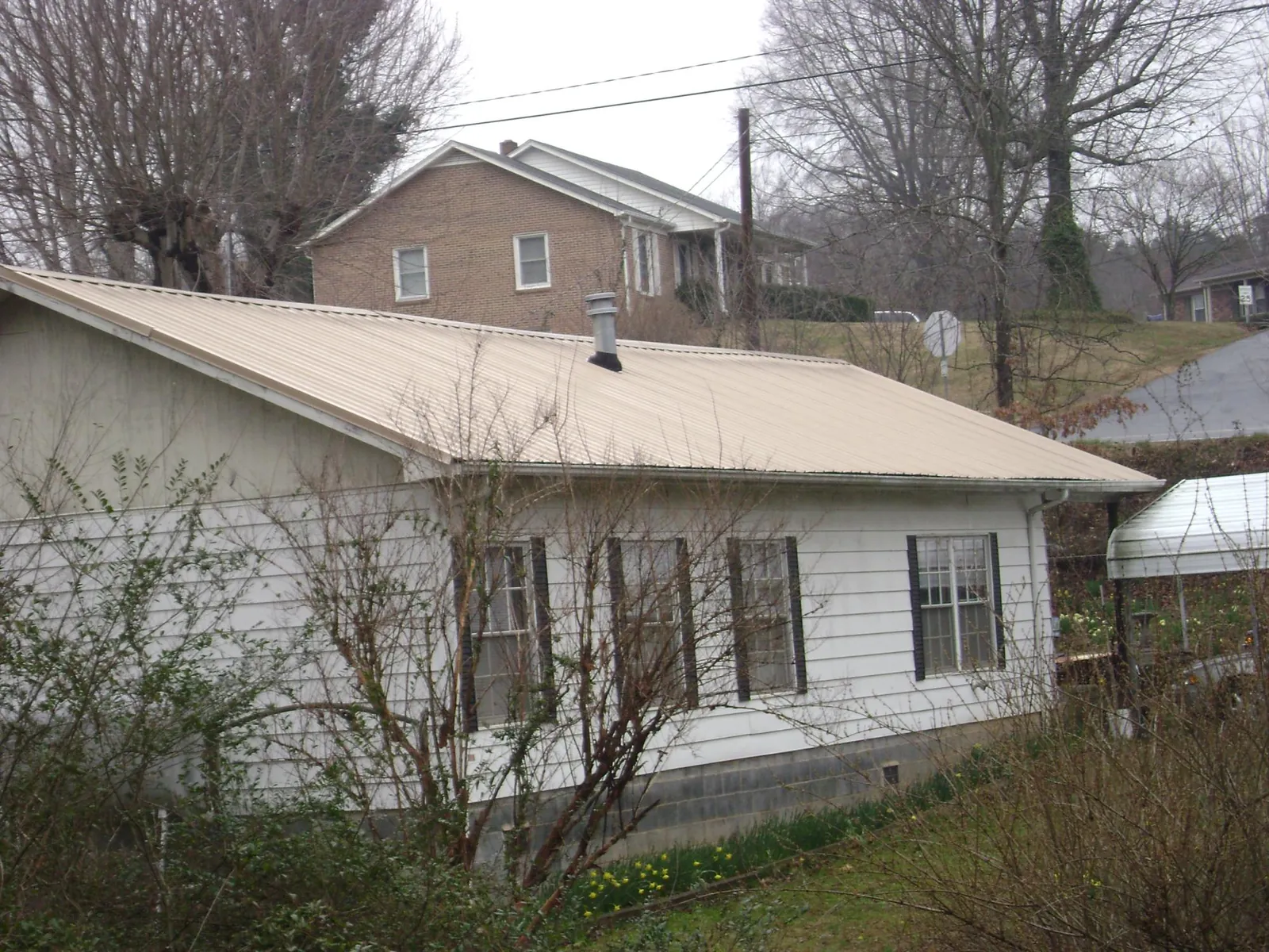 Tan metal roof on a white sided house set into a hillside — Commercial Roofing by Roofing Brothers in Stahlstown